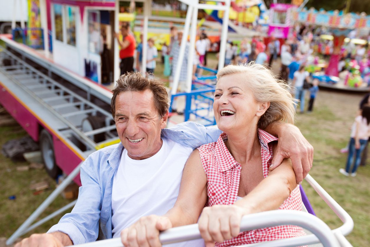 Playful dating Senior couple on a ride in amusement park Couple laughing and holding hands on a roller coaster ride at an amusement park, enjoying a playful and exciting date.
