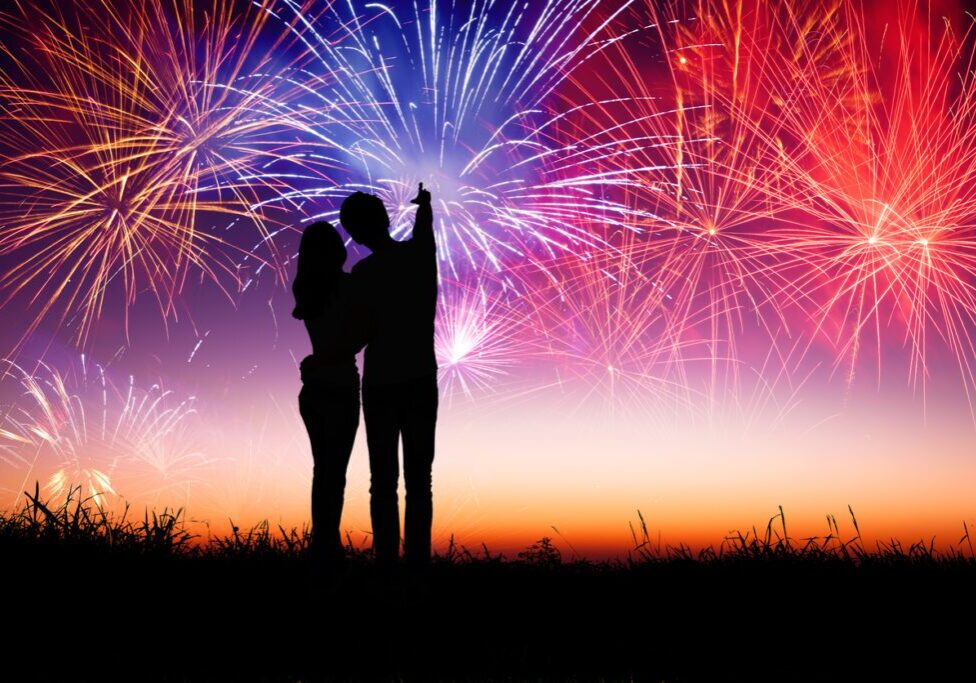 A romantic couple stands close while watching fireworks light up the sky — capturing the thrill of early chemistry in dating and the emotional highs that often define the start of a relationship.