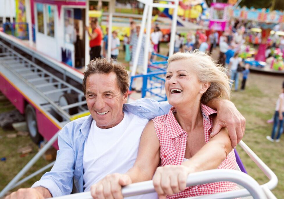 Couple laughing and holding hands on a roller coaster ride at an amusement park, enjoying a playful and exciting date.
